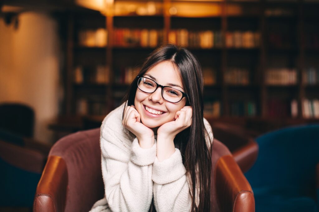 Smiling young woman in glasses at a library — beautiful smile maintained by Brookside Family Dentistry in O’Fallon