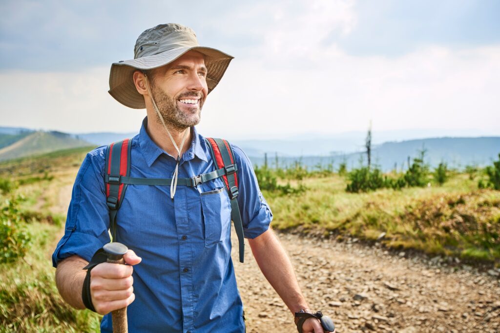 Man hiking on a trail with a sunhat and backpack, smiling at the view