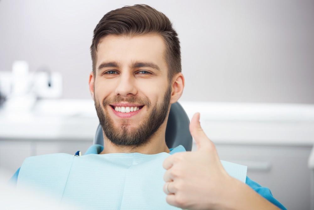 man smiling in dental chair after restoring a damaged tooth with a custom dental crown at Brookside Family Dentistry in O'Fallon, MO